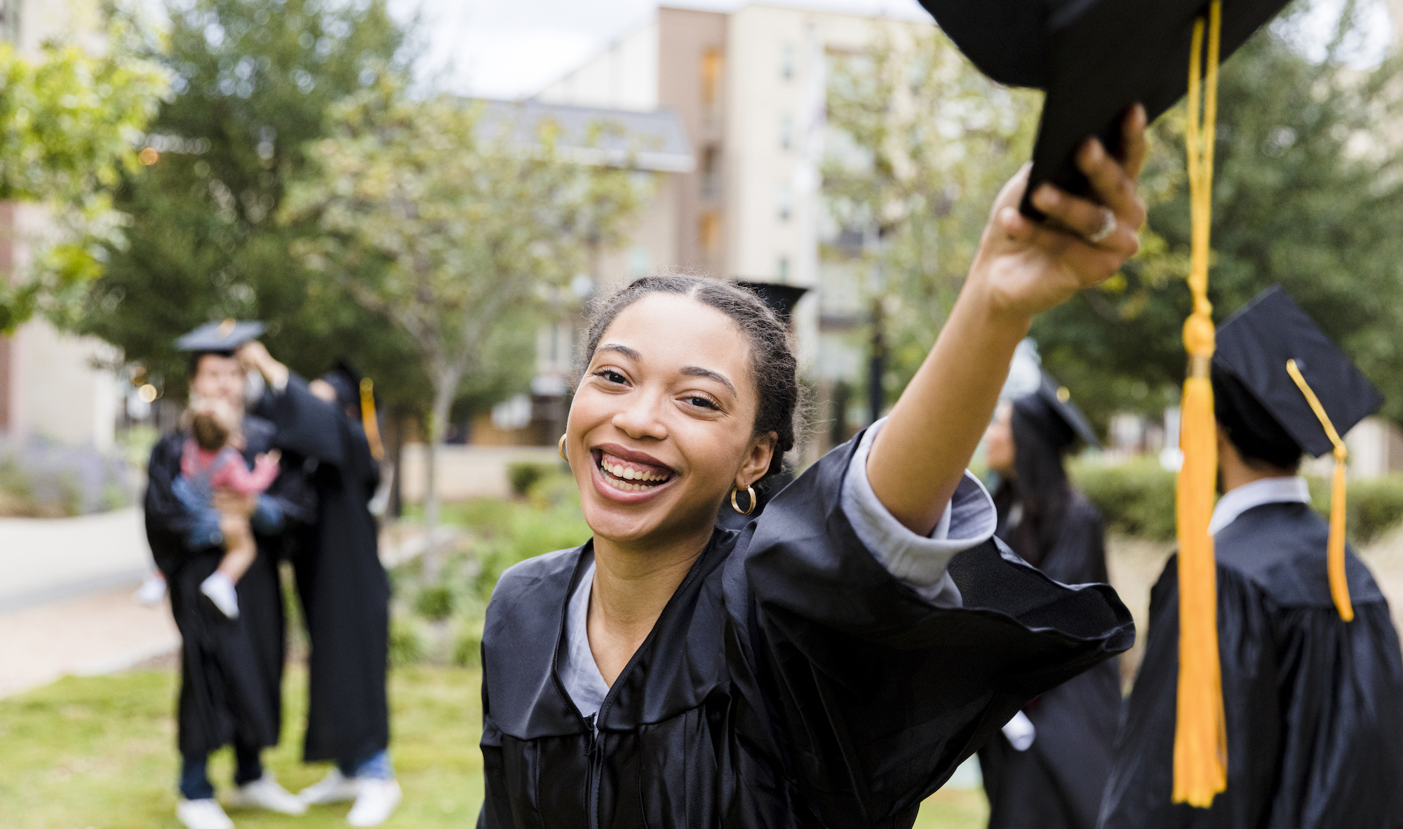 A young female graduate smiles at the camera while holding her mortarboard